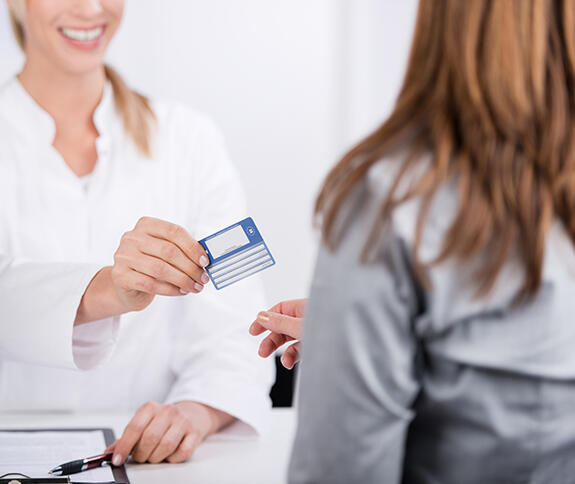 Frau im Laborkittel reicht einer Patientin ihre Versicherungskarte