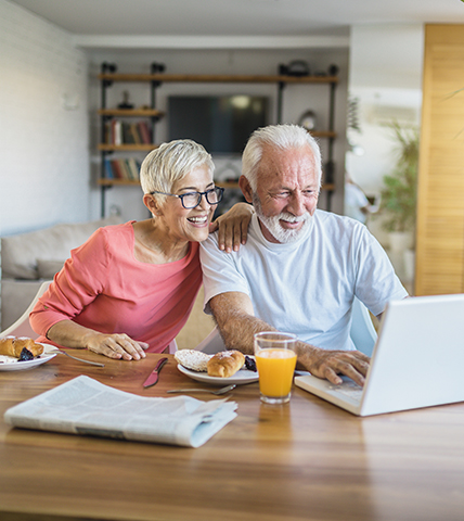 älterer Mann und ältere Frau schauen auf einen Laptop 