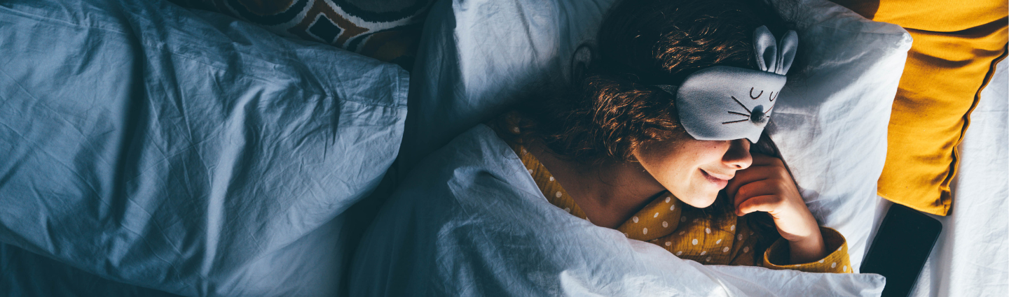 Junge Frau im Bett mit Schlafmaske